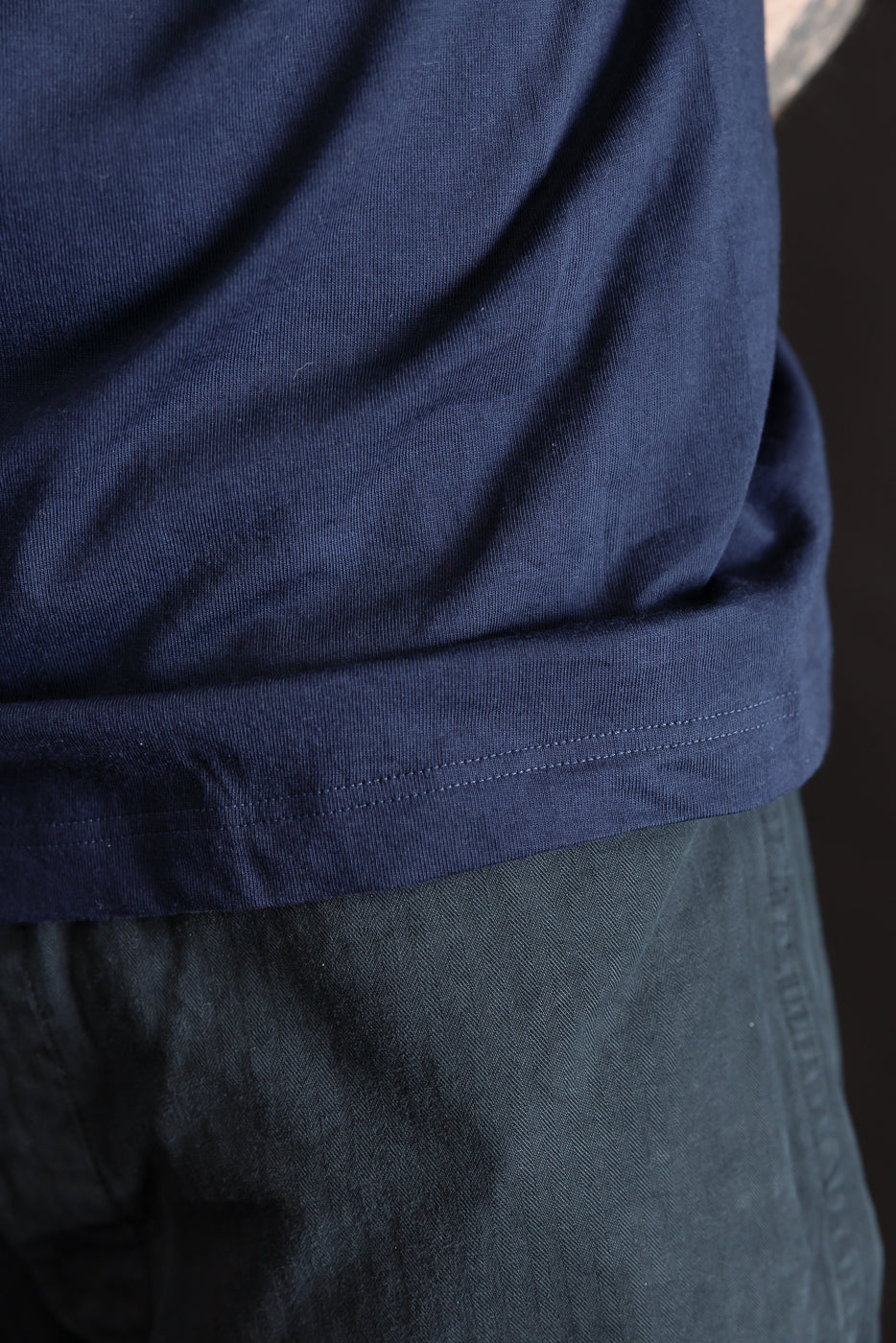 Close-up of hem and side seam on ink blue loopwheeled T-shirt, male model, left side view.