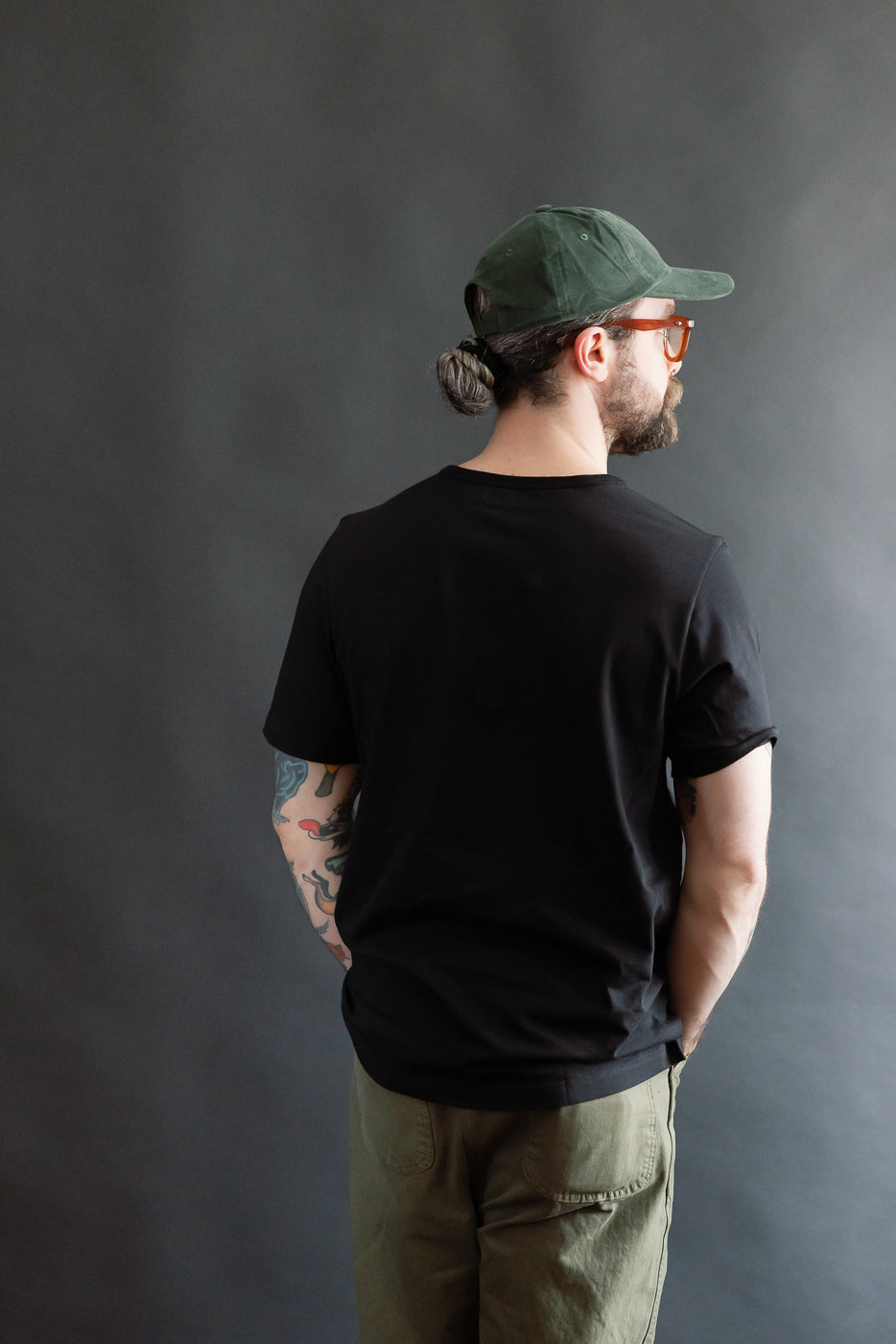 Back view of male model 5'9, 165lbs athletic build wearing deep black loopwheeled T-shirt and olive pants, Dant casual apparel.