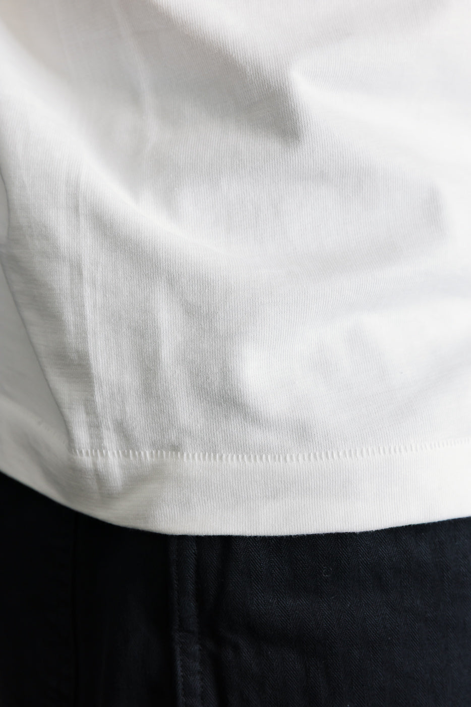 Close-up of white loopwheeled t-shirt hem showing fabric texture and stitching, front lower section.