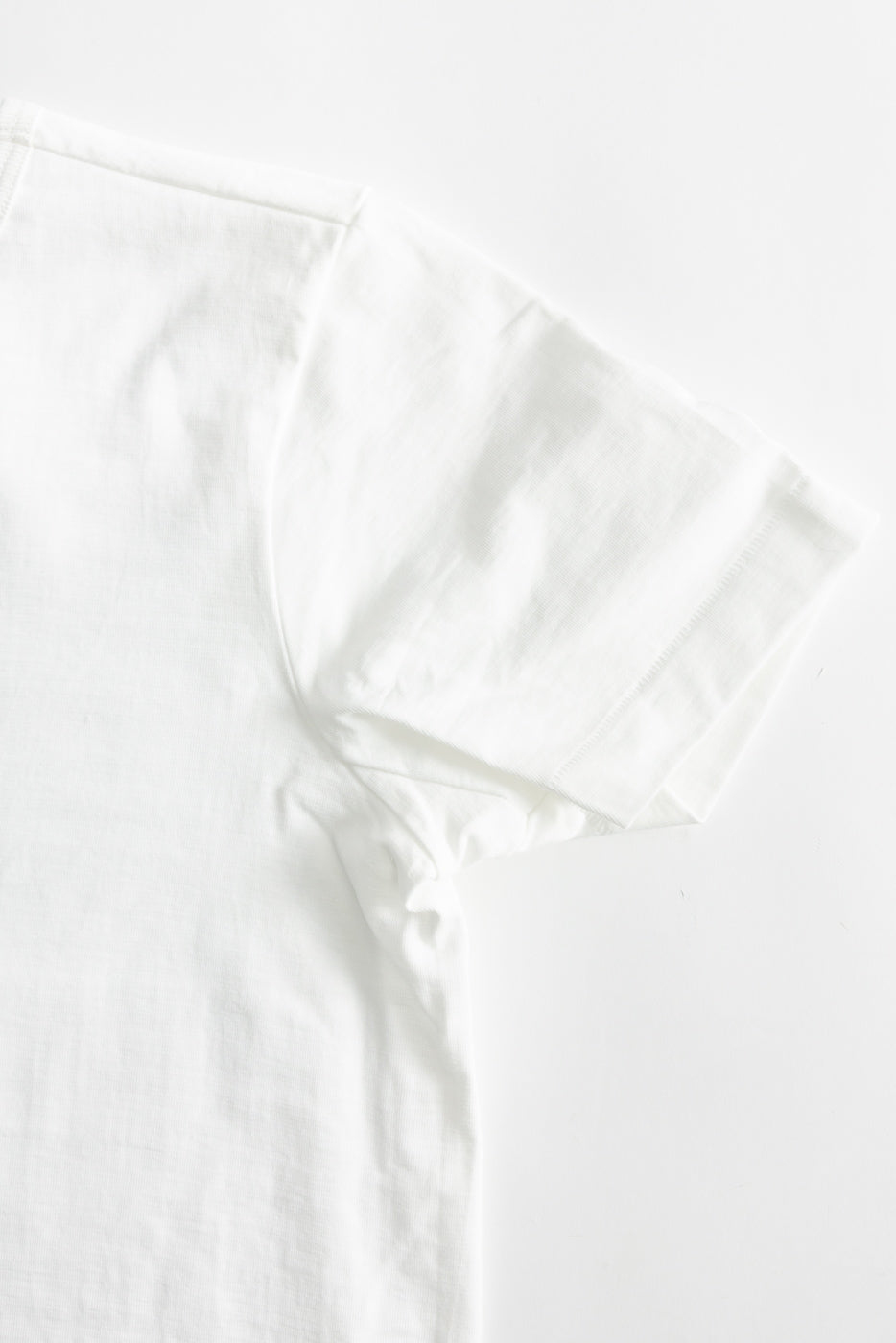 Close-up of white short sleeve loopwheeled t-shirt, back right shoulder and sleeve, fabric detail visible.