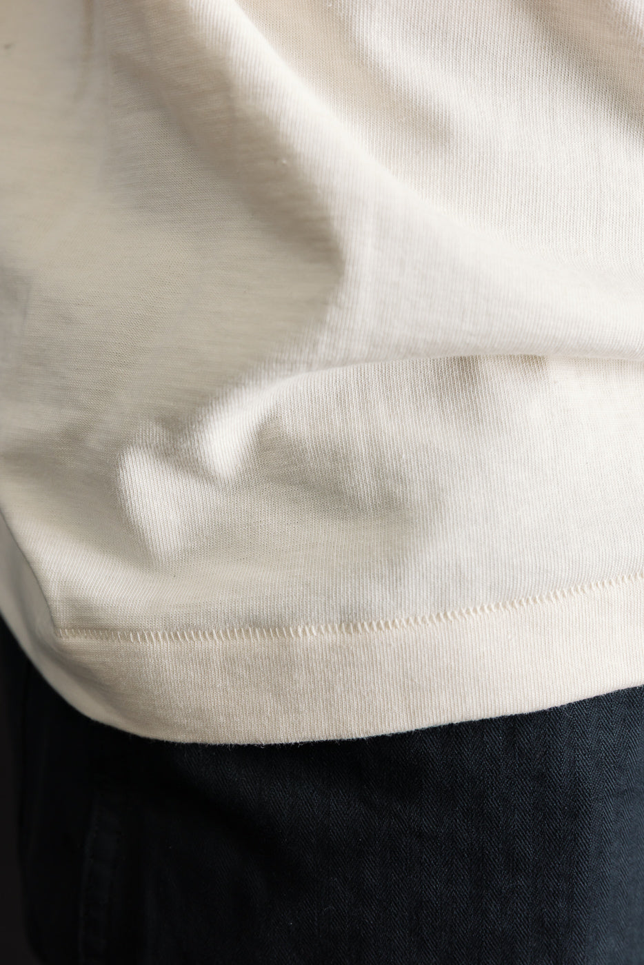 Close-up of men's natural color t-shirt hem and fabric texture, side view