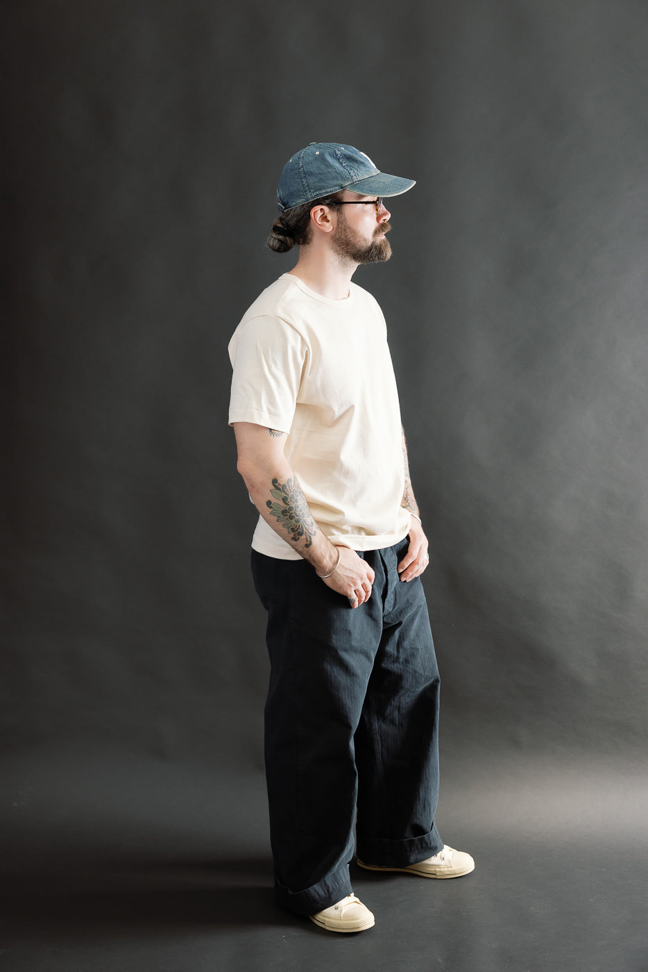 Full body side view of male model 5'9, 165lbs in athletic build wearing natural color loopwheeled classic fit t-shirt with short sleeves and dark wide-leg pants.