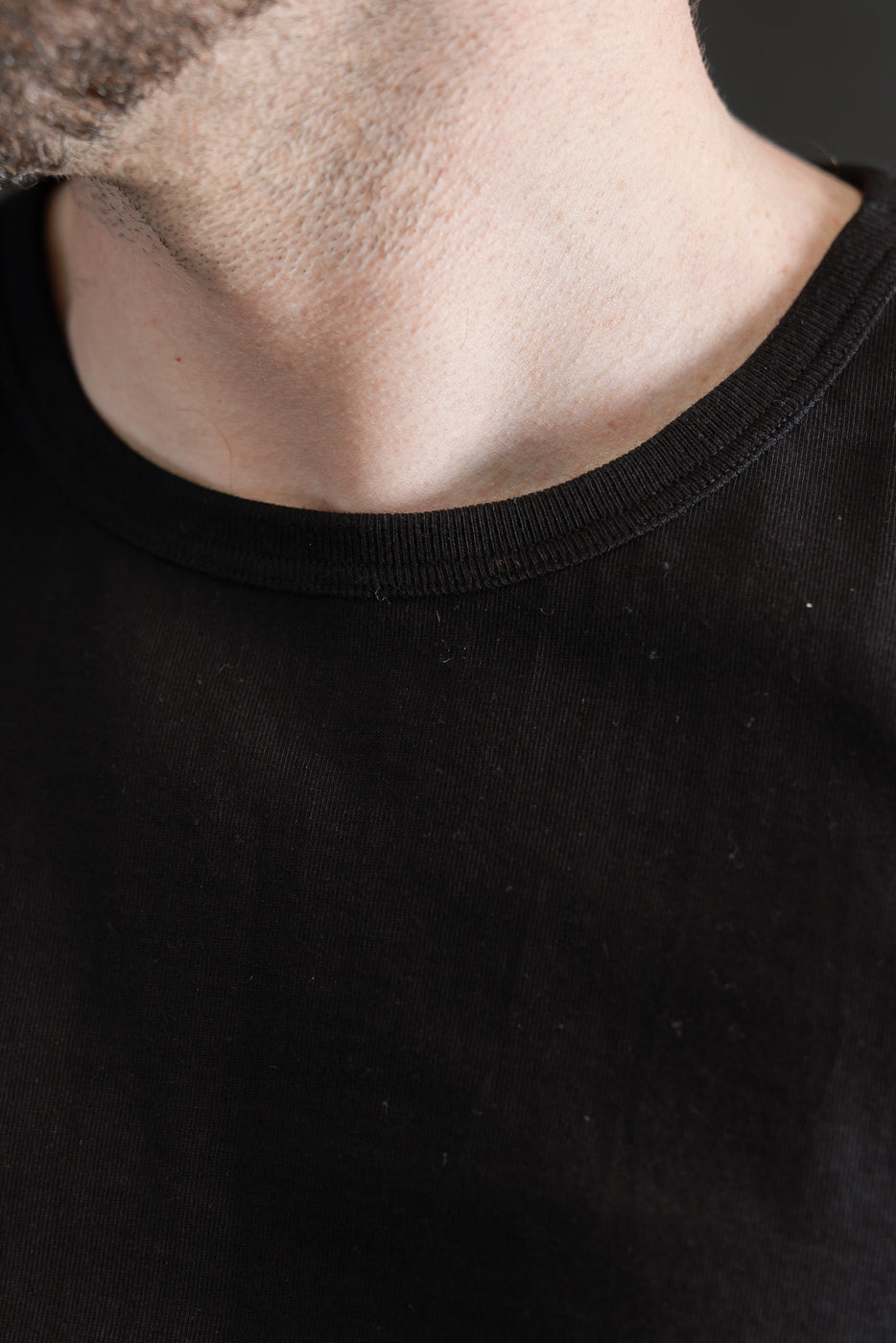 Close-up of a person wearing the 215.99 - 7.2oz Loopwheeled T-Shirt Classic Fit - Deep Black, highlighting its subtle textured fabric and comfortable fit around the neck and jawline area.