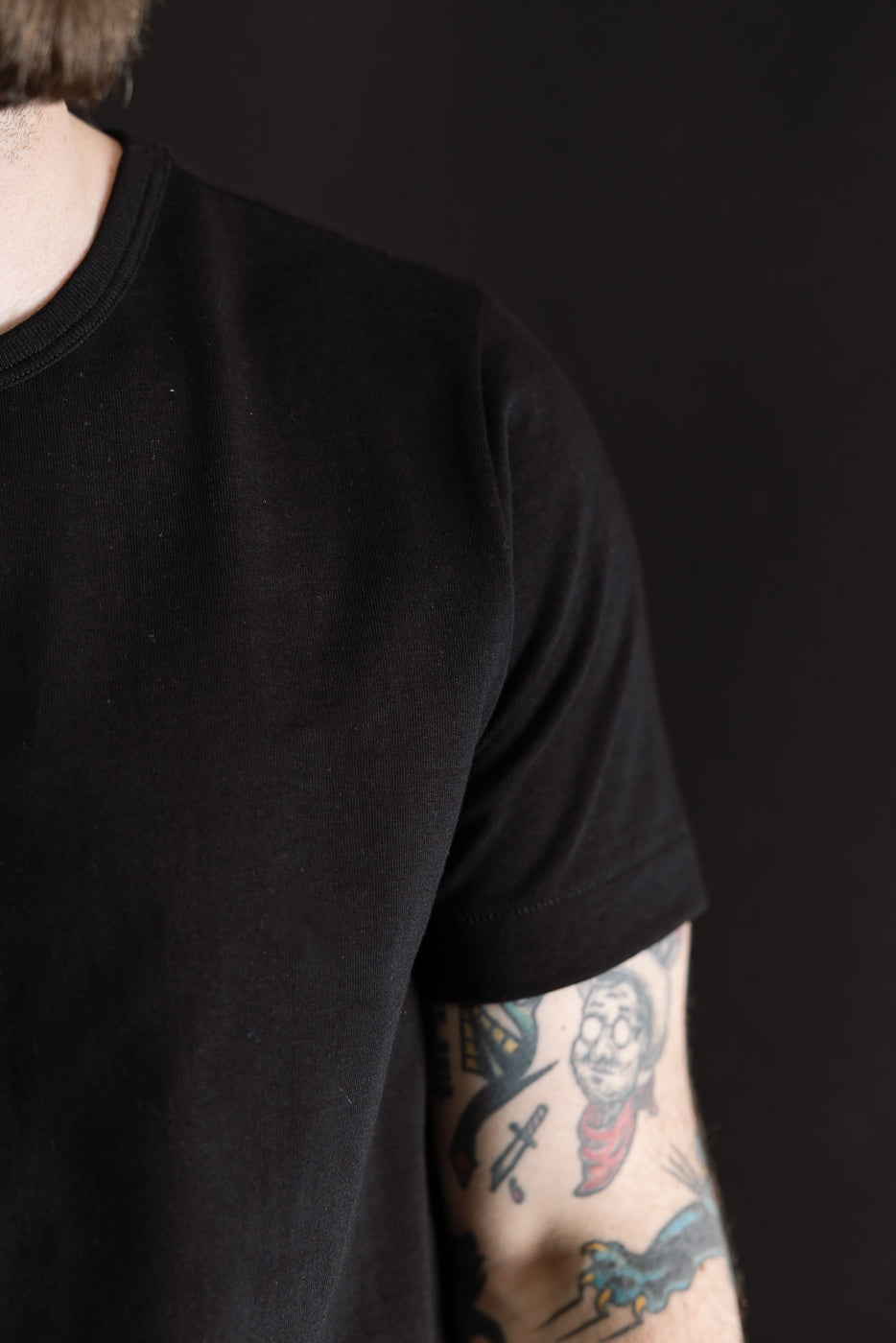 Person wearing 215.99 - 7.2oz Loopwheeled T-Shirt Classic Fit - Deep Black, showcasing textured fabric with exposed tattooed arm; captures premium menswear essence from Dant's curated collection.