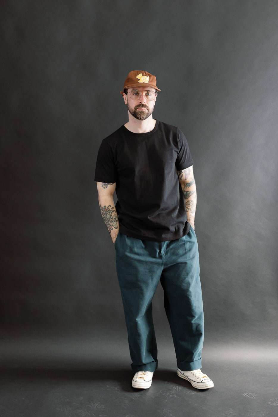 Model wears 215.99 - 7.2oz Loopwheeled T-Shirt Classic Fit - Deep Black; features subtle textured fabric and classic fit, styled with teal trousers and white sneakers, reflecting Dant's premium menswear ethos.