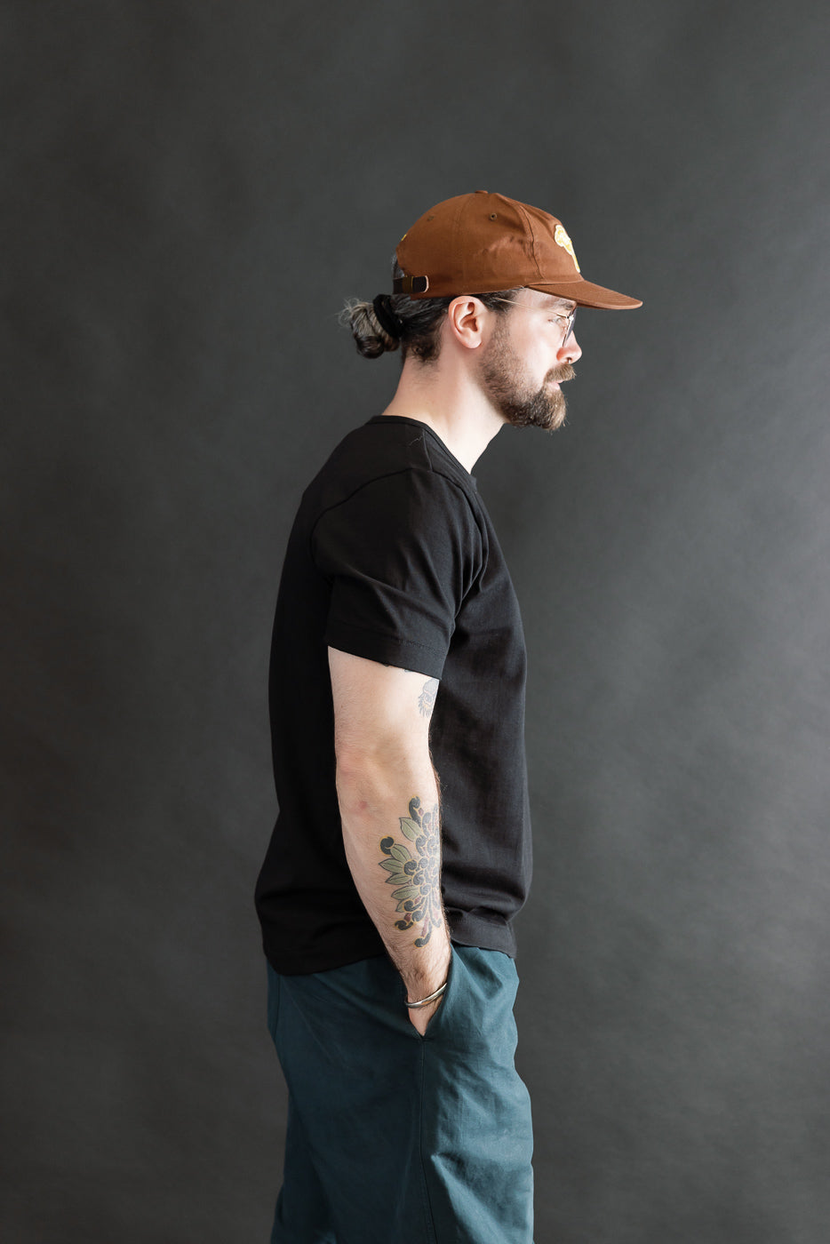 Man in profile wearing 215.99 - 7.2oz Loopwheeled T-Shirt Classic Fit - Deep Black, showcasing its classic fit and textured fabric. His tattooed arm highlights the tee's comfort and iconic status.