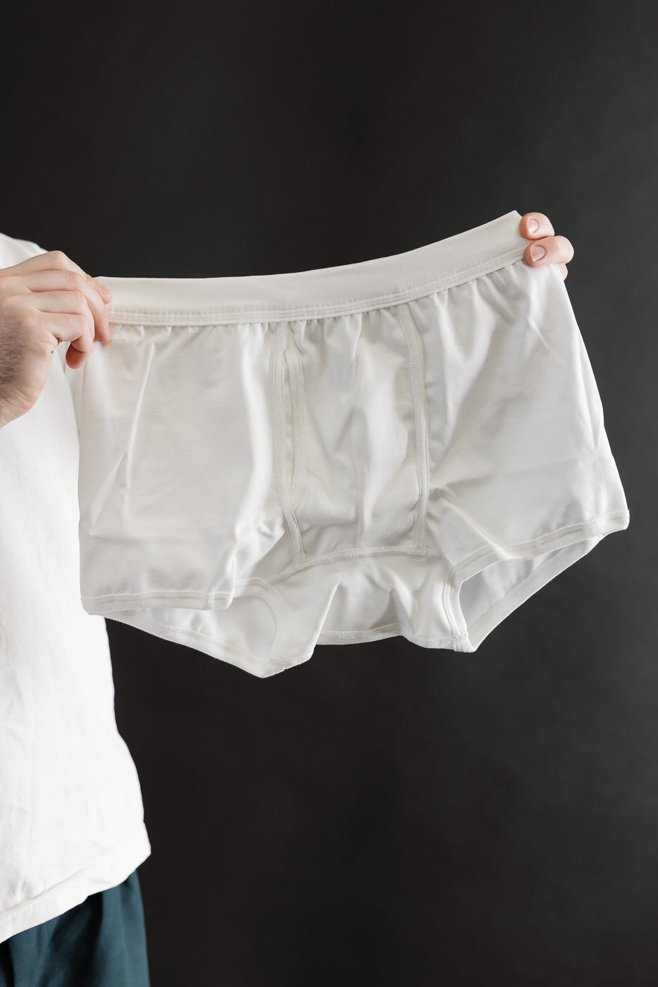 Close-up front view of white loopwheeled boxer brief held by male model, elastic waistband visible.