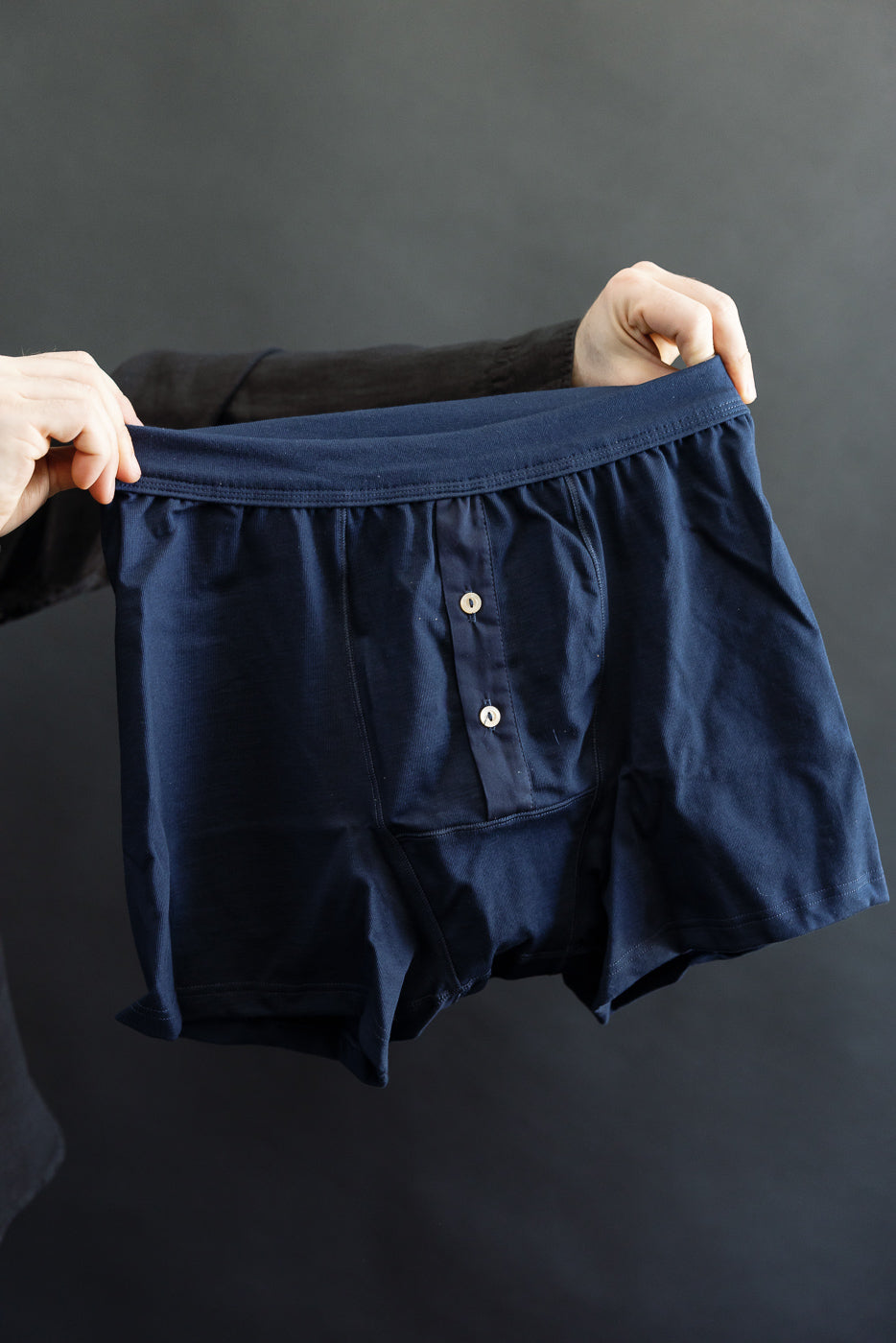 255.66 - Loopwheeled Boxer Button Fly - Ink Blue, showcased against a dark backdrop, features a navy-blue boxer-style design with a two-button fly and elastic waistband, crafted from 100% organic cotton.