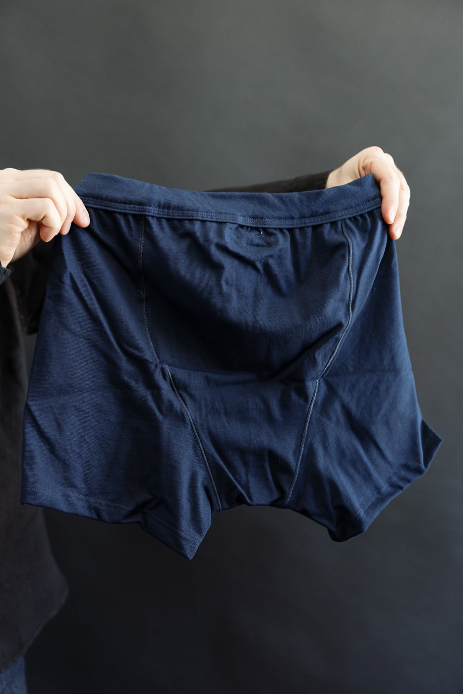 Person holding navy-blue 255.66 - Loopwheeled Boxer Button Fly with visible waistband and contoured seams against a neutral background, showcasing the premium fabric and craftsmanship from Dant's collection.
