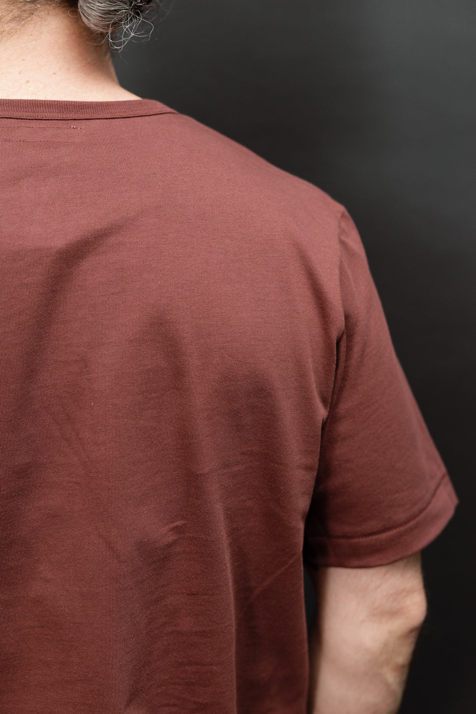 Close-up back view of a male model's brown cotton t-shirt showing fabric texture and neckline.