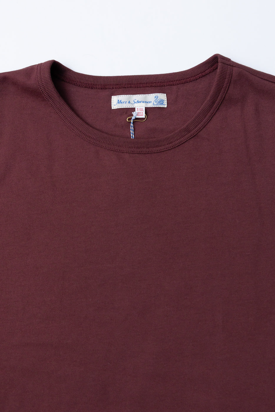 Close-up of the front neckline and brand tag of a burgundy t-shirt.
