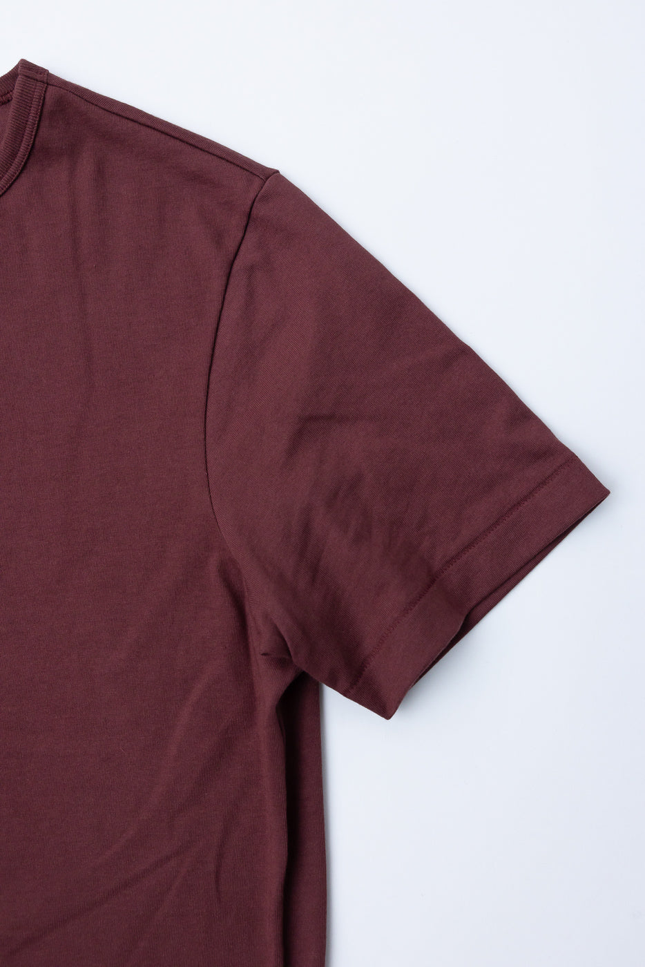 Close-up of the front right shoulder and short sleeve of a maroon cotton t-shirt.