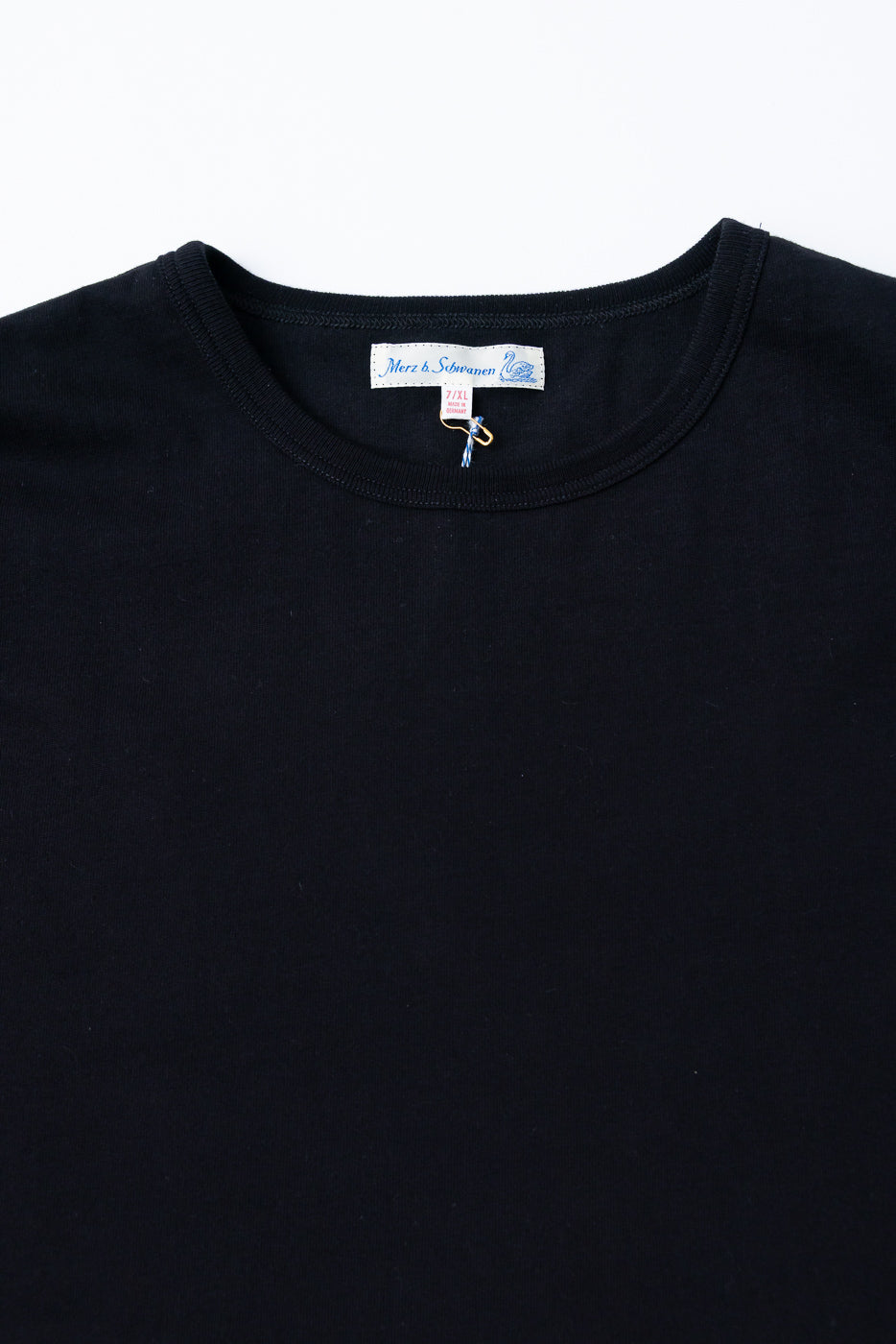 Close-up front view of a black crewneck t-shirt showing the neckline and Merz b. Schwanen tag.