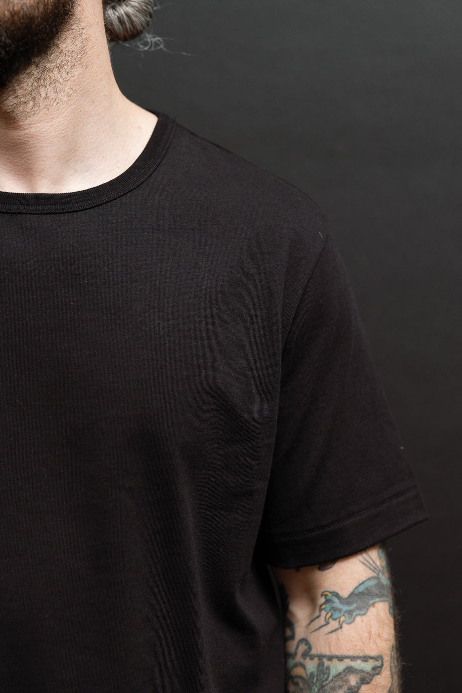 Close-up of the left side and sleeve of a black cotton crewneck t-shirt on a male model.