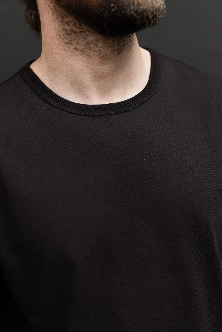 Close-up front view of a black crewneck t-shirt's ribbed collar and fabric texture on a male model.