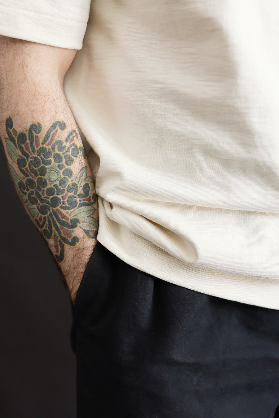 Close-up of a torso showcasing the 2S14.02 - 10.7oz Loopwheeled Heavy T-Shirt Relaxed Fit - Nature, highlighting its slightly tucked design, relaxed fit, and the prominent floral tattoo on the forearm.