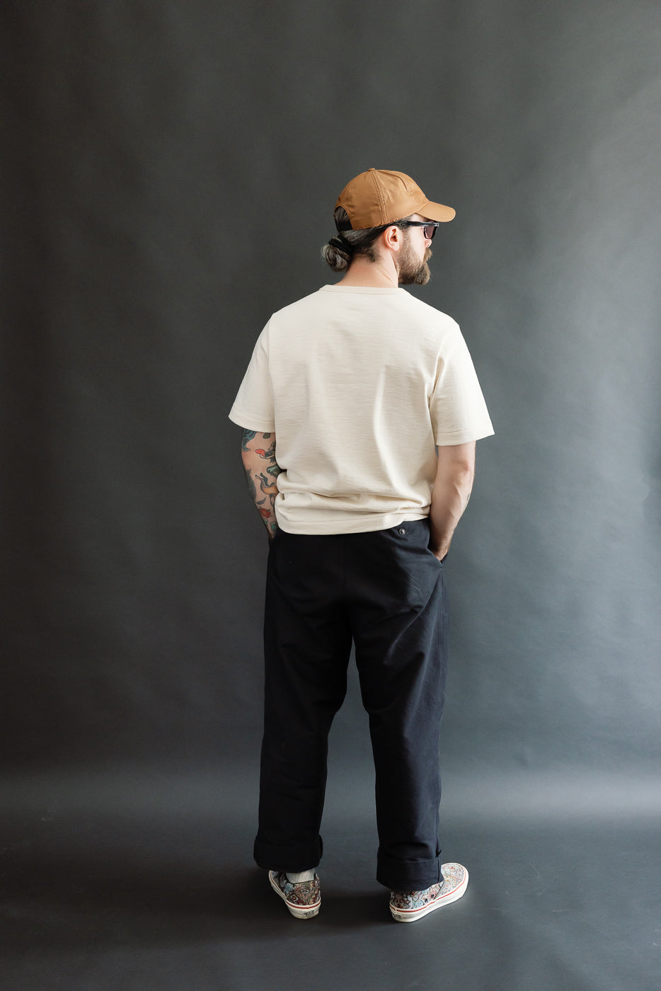 Man wearing 2S14.02 - 10.7oz Loopwheeled Heavy T-Shirt Relaxed Fit - Nature, showcasing its relaxed fit, detailed neckline, and casual slub structure, paired with black trousers and patterned sneakers.