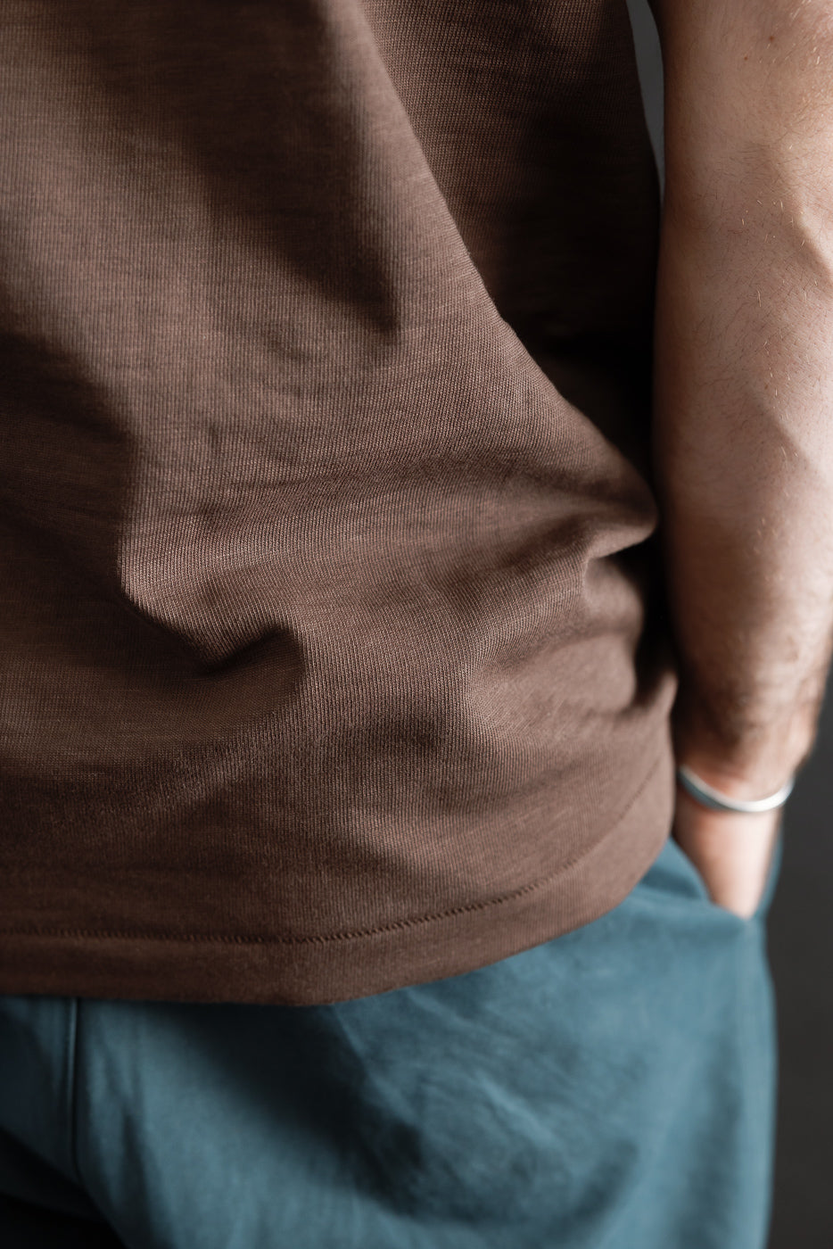 Close-up of male model's right side hem and fabric texture on chocolate brown heavy t-shirt.
