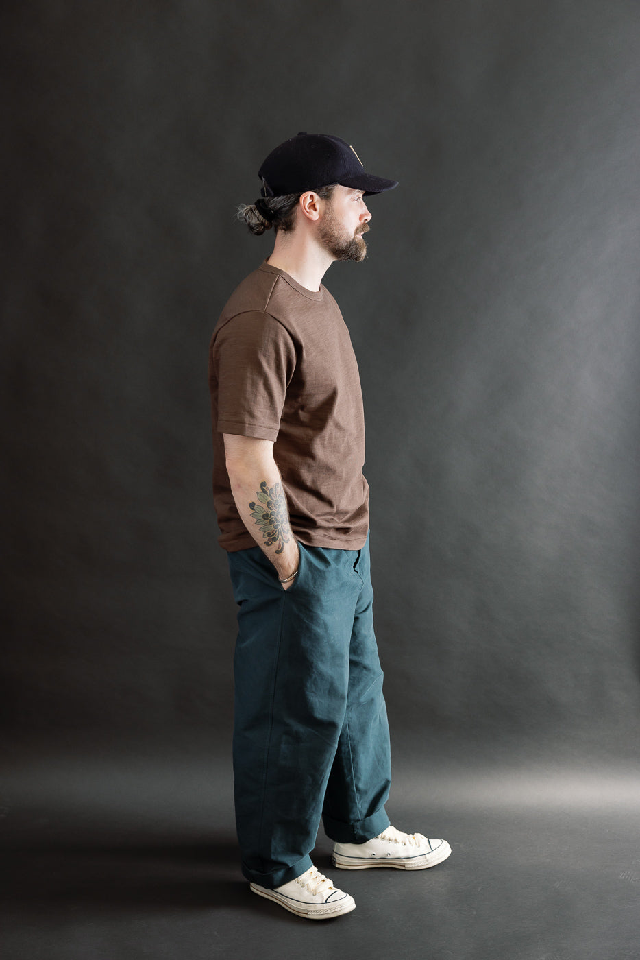 Full body side view of male model 5'9 165lbs athletic build wearing relaxed fit chocolate heavy T-shirt and teal pants