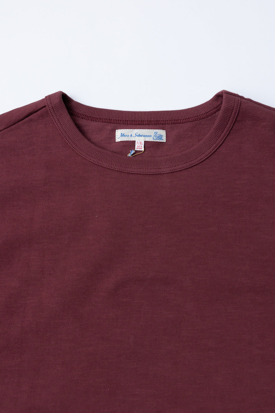 Close-up of the front neckline and tag of a burgundy crewneck t-shirt.
