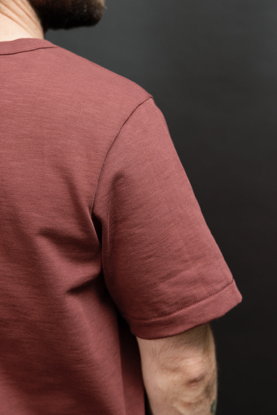 Close-up of the right sleeve and shoulder of a male model's mauve cotton t-shirt.