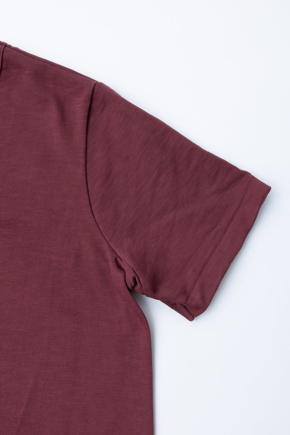 Close-up of the right sleeve and shoulder seam of a maroon textured cotton t-shirt.