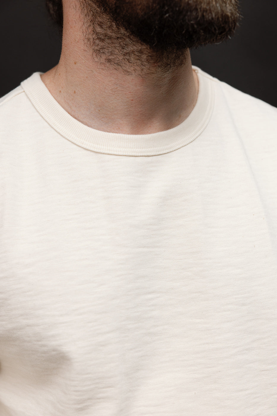 Close-up front view of the ribbed crewneck collar and textured fabric of a white t-shirt.