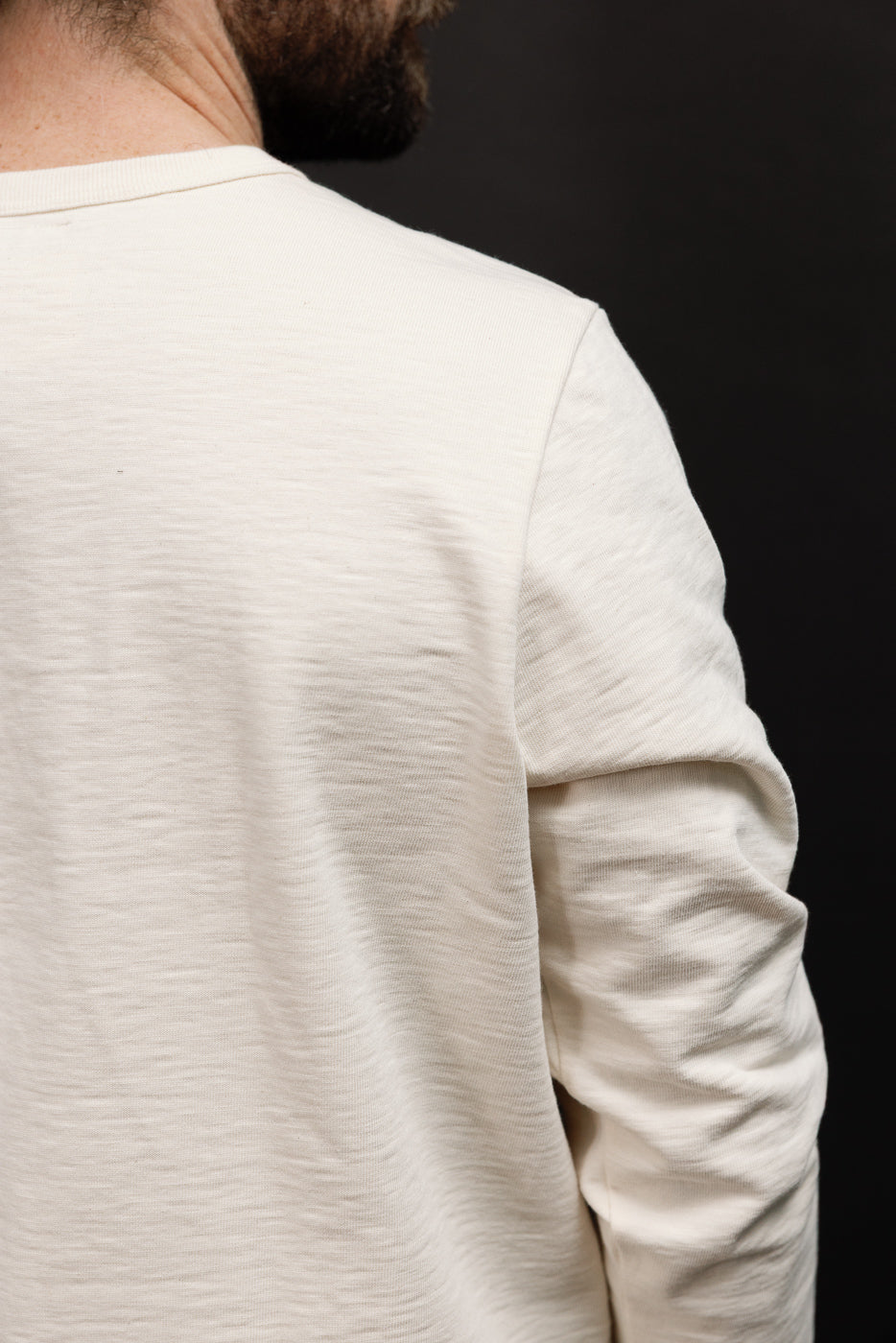 Close-up of the back and right sleeve of a white textured long-sleeve shirt on a male model.