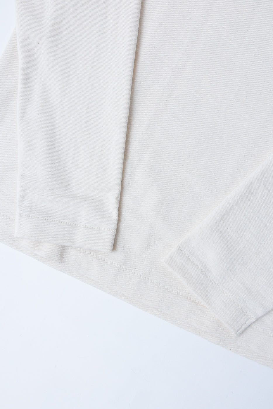 Close-up of the front hem and sleeve of a white long-sleeve cotton shirt.