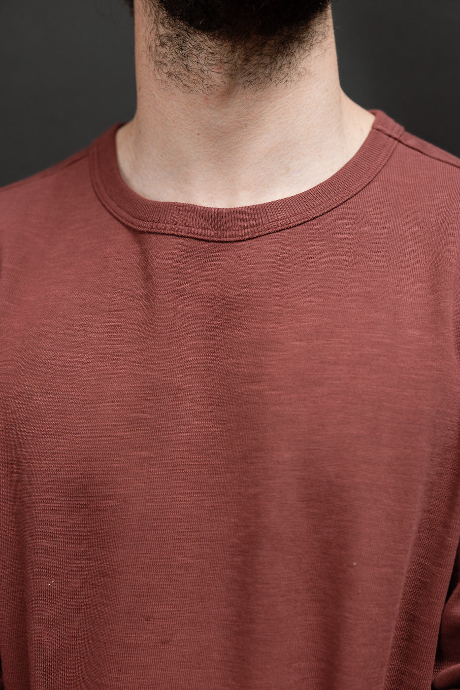 Close-up front view of the crew neck and fabric texture of a male model's brown t-shirt.