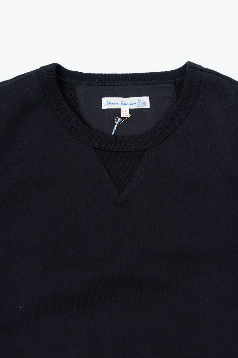 Close-up front view of the ribbed crewneck and tag of a black knit sweater.