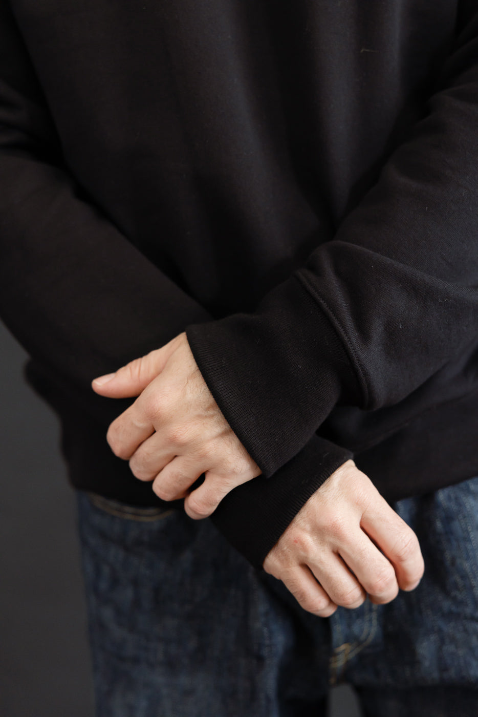 Close-up of the ribbed cuff and sleeve of a black sweatshirt worn by a male model.