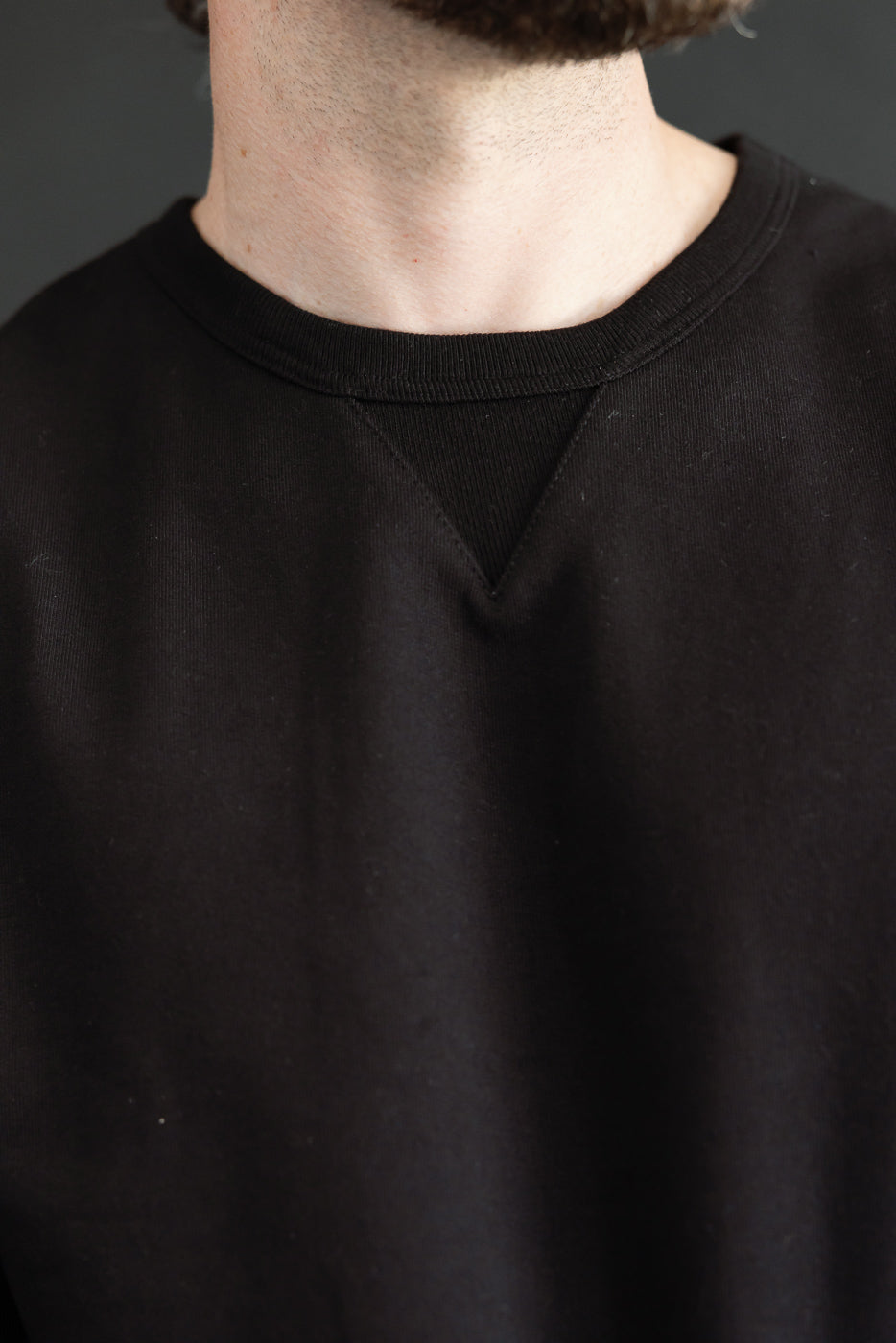 Close-up front view of a black crewneck sweatshirt showing the ribbed collar and V-stitch detail.