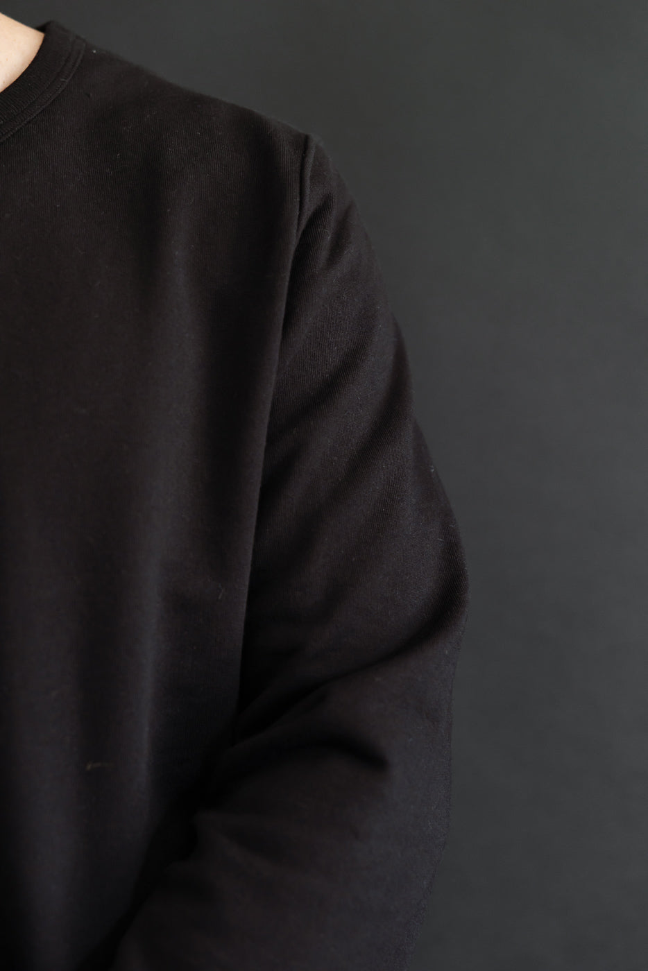 Close-up side view of a black long-sleeve sweatshirt showing the sleeve and shoulder fabric texture.