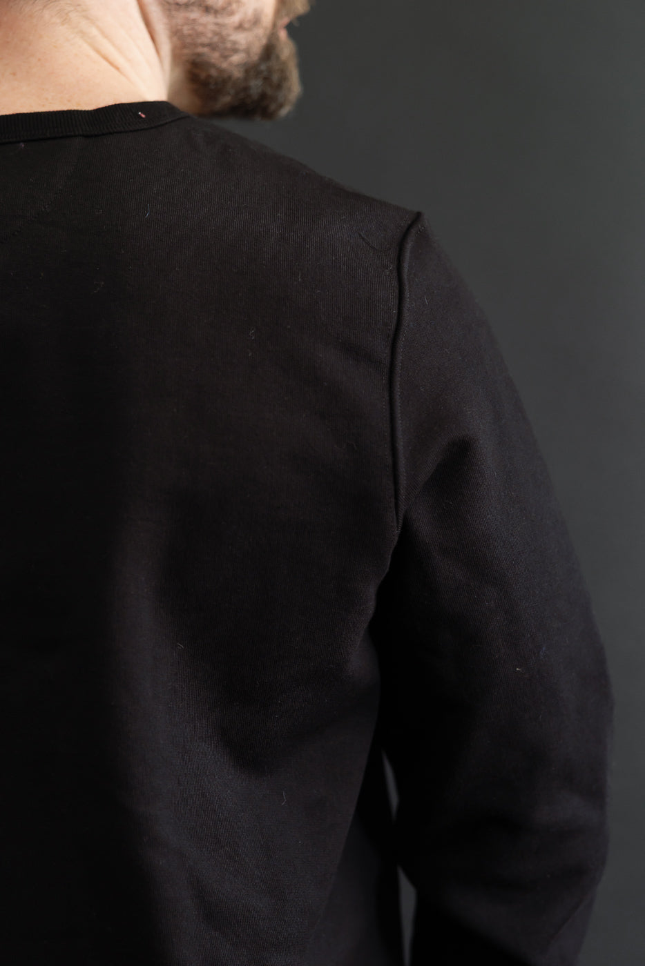 Close-up back view of a black long-sleeve sweatshirt showing shoulder seam and fabric texture.