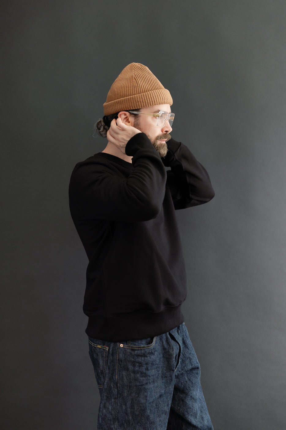 Side view of a male model wearing a black sweatshirt and denim jeans against a gray background.
