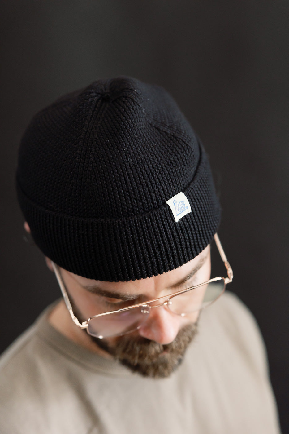 Close-up of Merz b. Schwanen deep black ribbed merino wool beanie front, worn by male model 5'9, 165lbs, athletic build, tag visible, Dant collection.