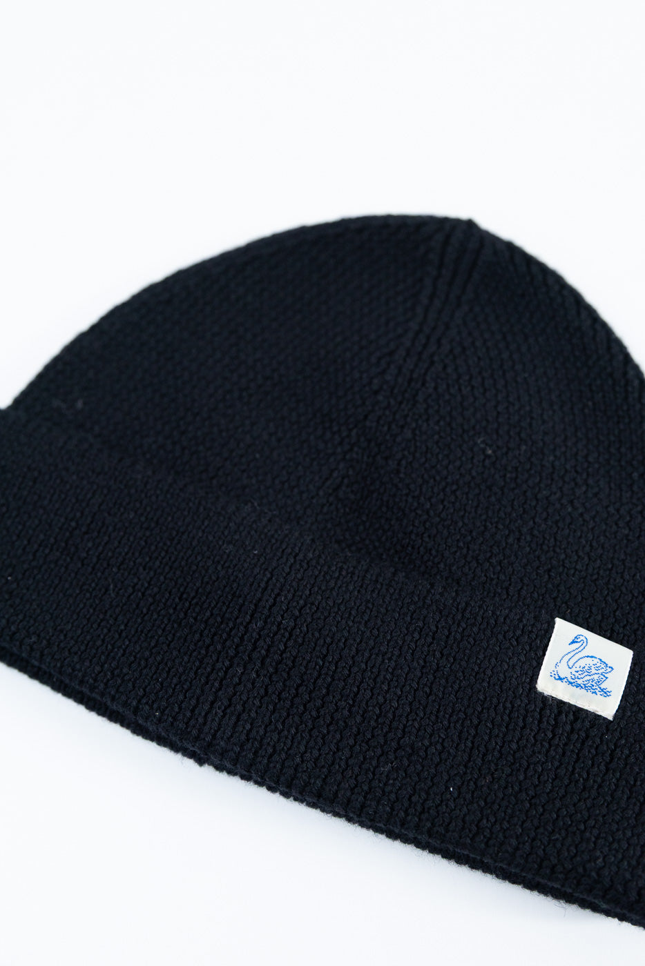 Close-up of front of deep black Merz B Schwanen ribbed merino wool beanie, swan logo tag visible.