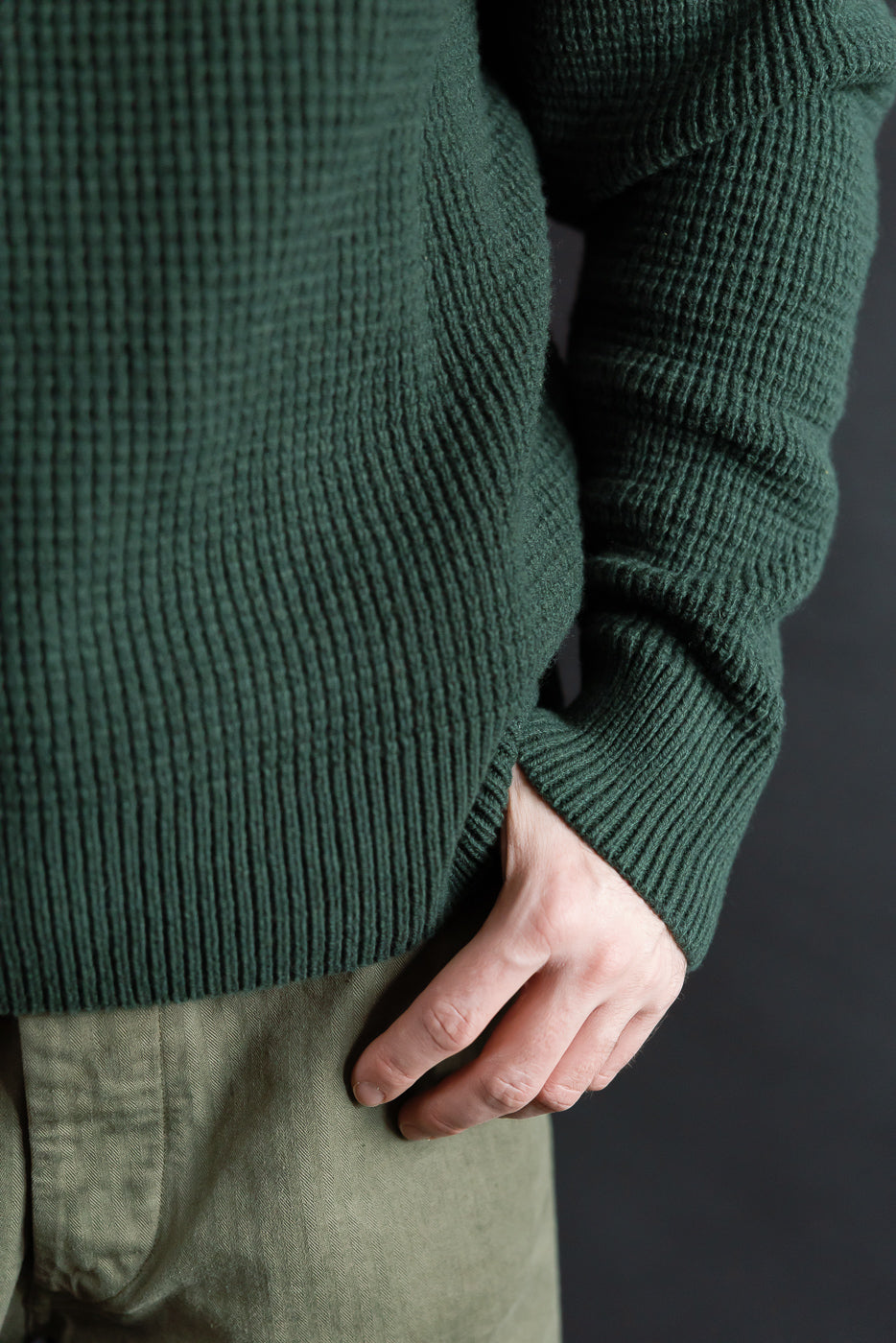 Close-up front of merino wool cashmere blend waffle pullover, bottle green, on male model, highlighting textured knit and ribbed hem.