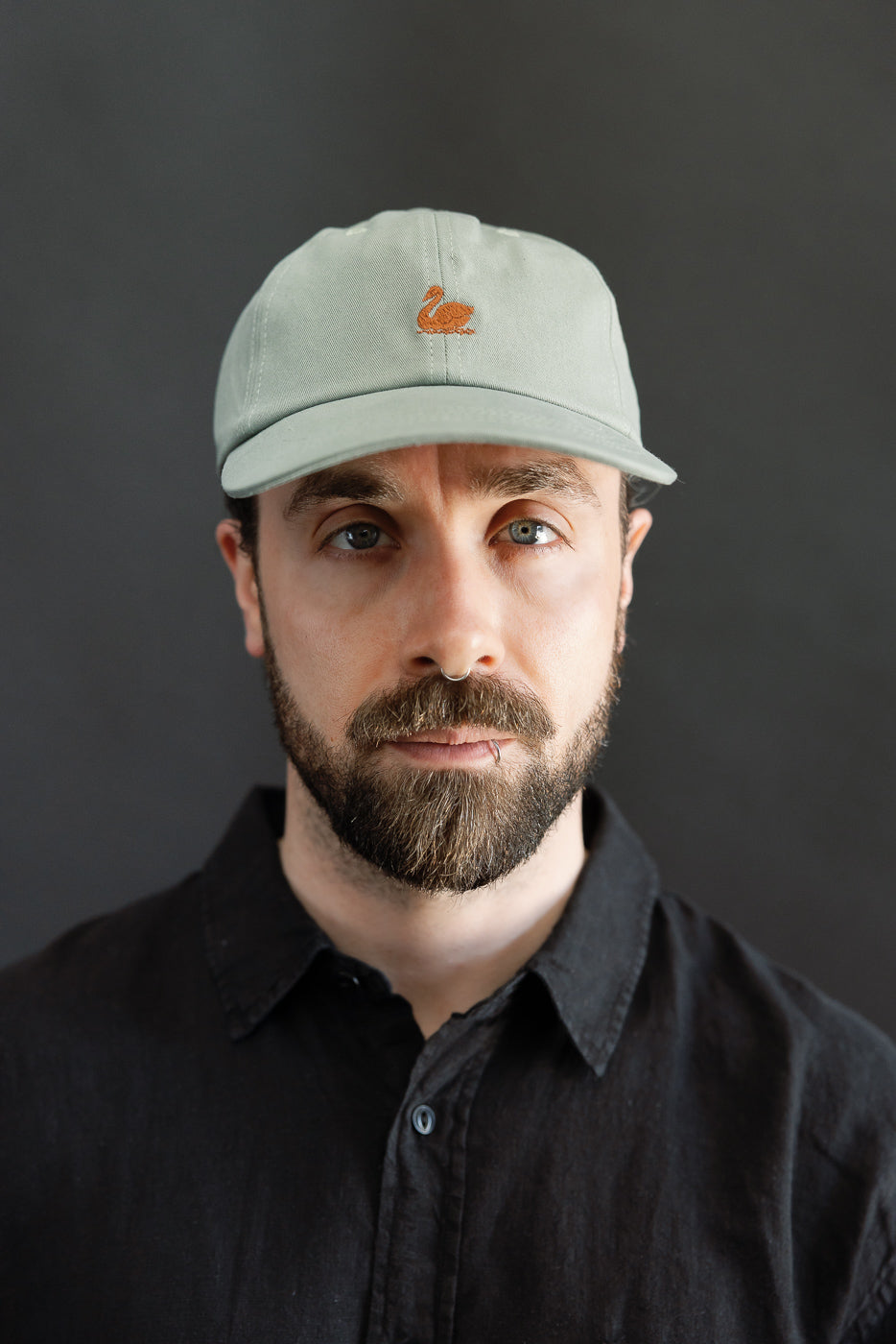 Close-up front view of light army cotton twill cap with swan logo on male model, 5'9