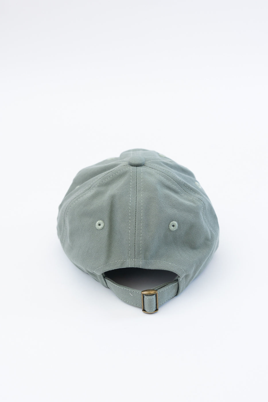 Close-up of back of light army green cotton twill cap with brass adjustable strap detail.