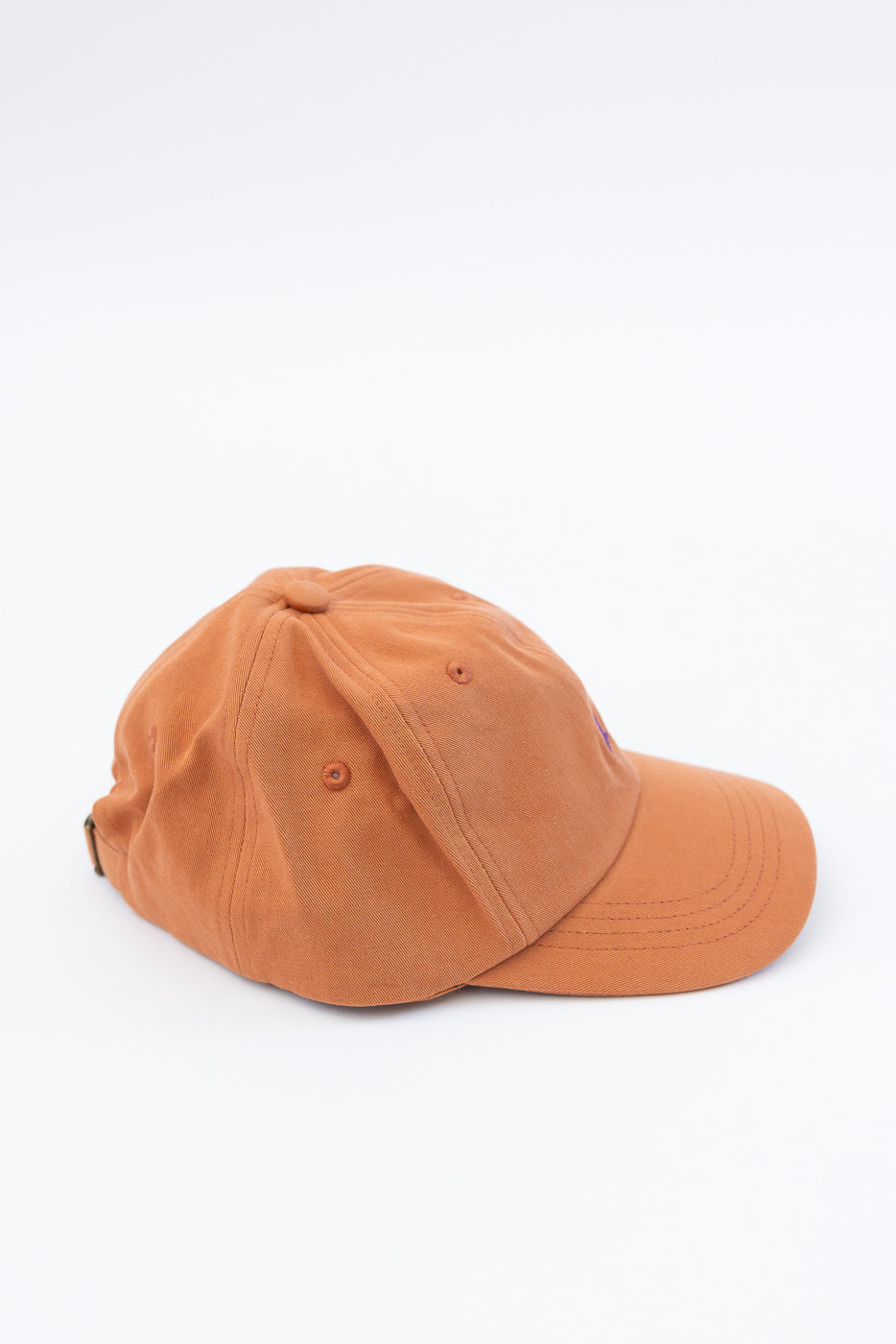 Close-up side view of pumpkin orange cotton twill cap showing top panels and stitching.