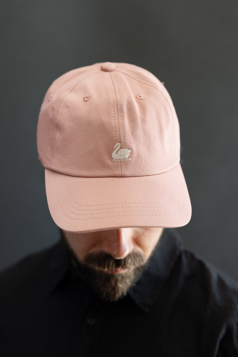 Close-up front view of rosewood cotton twill cap with swan logo, worn by male model 5'9