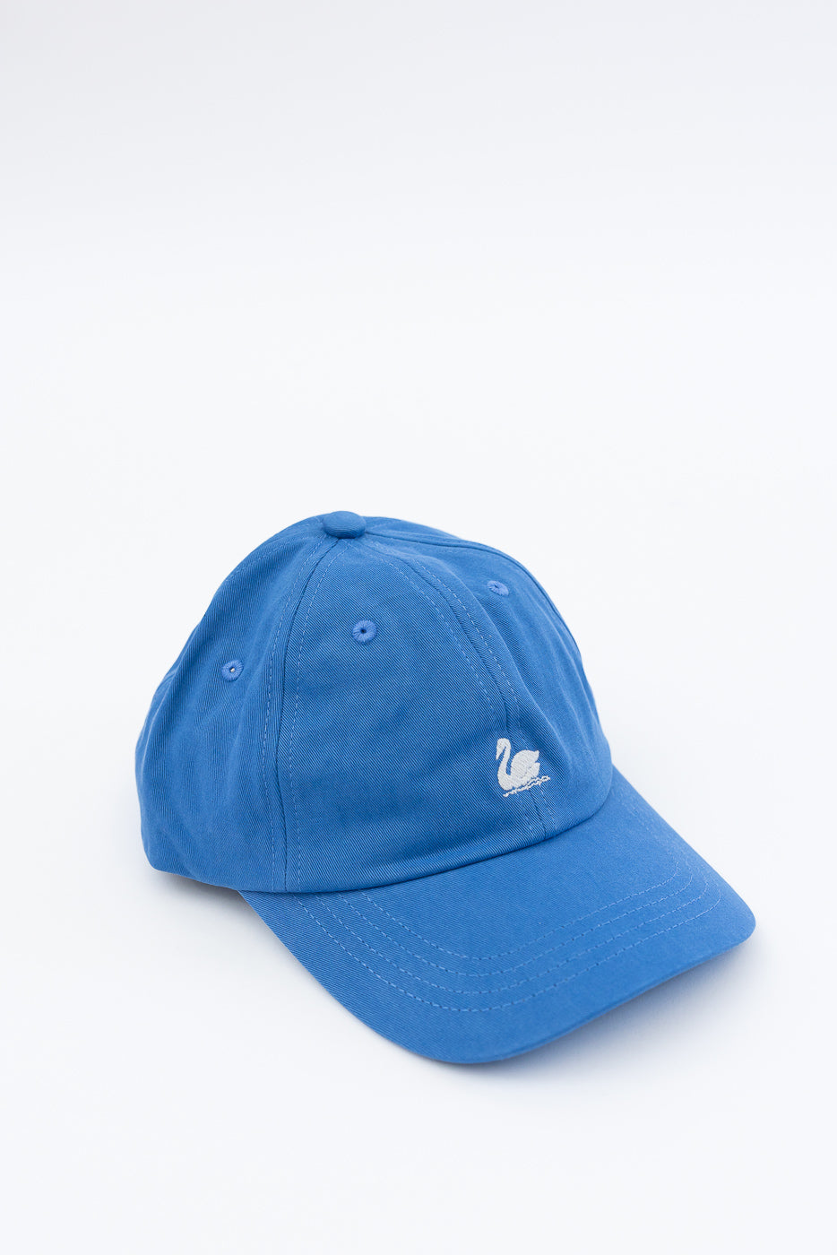 Front angled close-up of washed blue cotton twill cap with white swan logo embroidery.