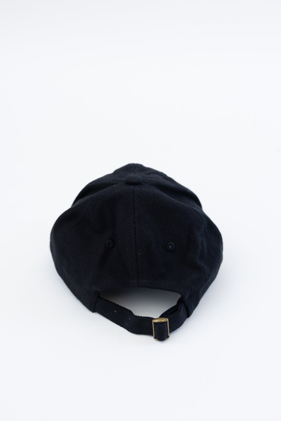 Close-up of the back of a black cotton twill cap showing strap and metal buckle.