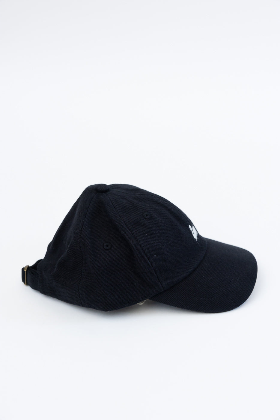 Side view close-up of deep black cotton twill cap featuring white swan logo and brass buckle.
