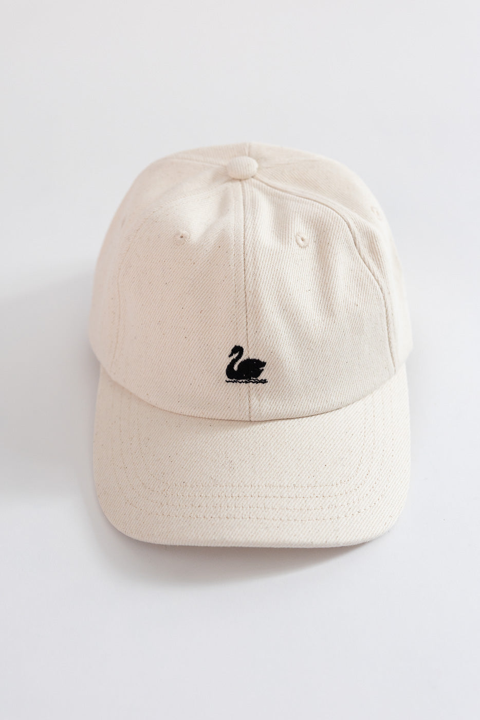Front close-up of cream cotton twill cap with black swan logo, flat lay, Dant accessories