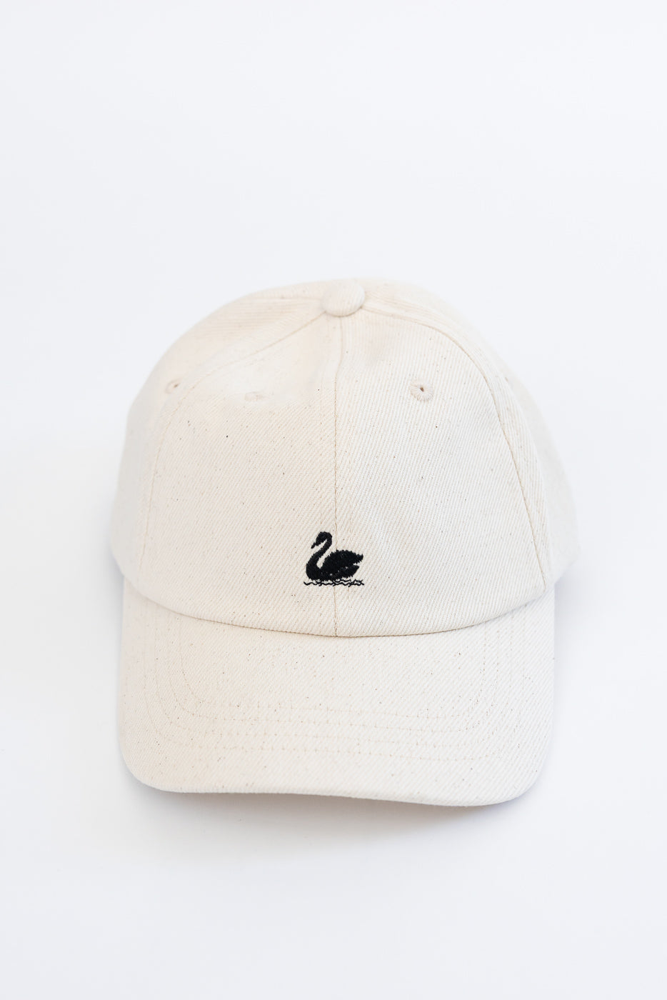 Front close-up of natural cotton twill cap with black swan logo embroidery, visor visible.
