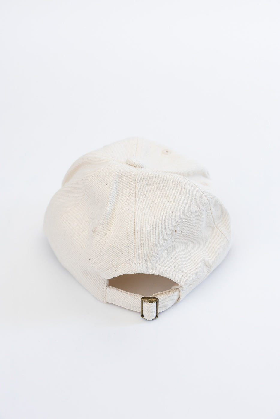 Close-up of natural cotton twill cap, back view showing adjustable metal strap detail.