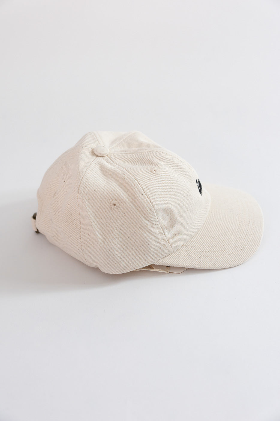 Close-up side view of Merz b. Schwanen cotton twill cap in natural white, showing top and bill.